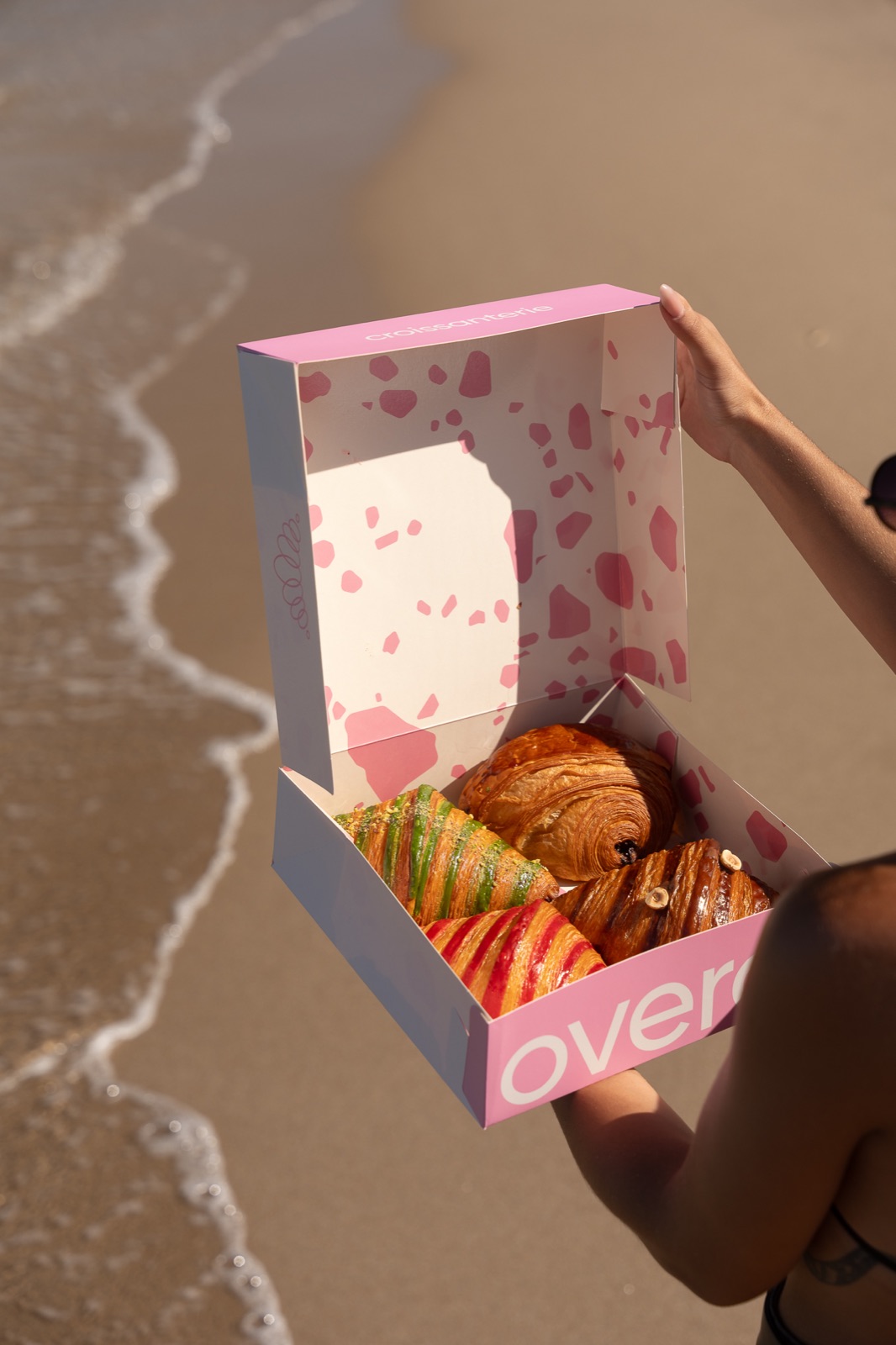 Ροζ κουτί Overoll με pastries δίπλα στη θάλασσα